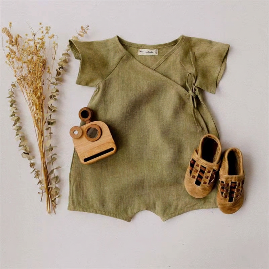 Khaki linen baby romper flat lay with dried flower bunch and wooden ring