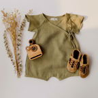 Army green linen baby romper with dried flowers and wooden toy