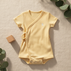 Lemon yellow baby romper laid flat on linen with wooden toy block and eucalyptus