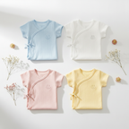 Four baby rompers in sky blue, white, blush pink and lemon yellow arranged in flat lay