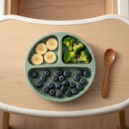 Sage green silicone divided plate with banana, broccoli and blueberries on high chair tray